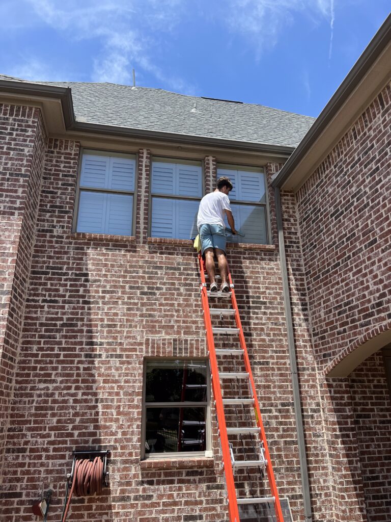 hwc1 Mean Green window cleaner on a ladder cleaning second story windows on a home in Dallas-Fort Worth