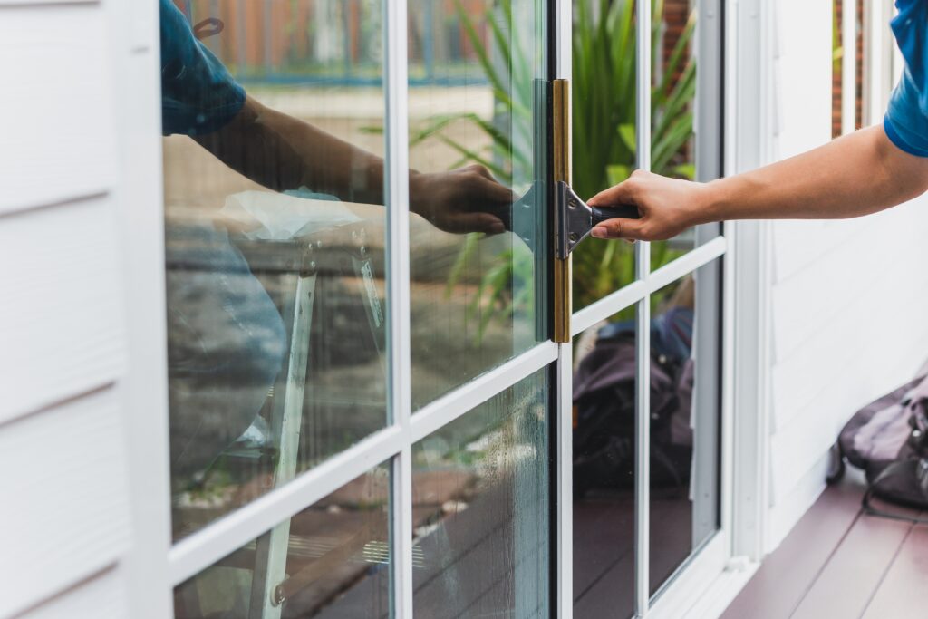 Worker,Use,Scraper,Cleaning,Window,Before,Installing,Tinting,Film. Mean Green Window Cleaning wiping down a home's windows in Dallas Fort Worth, Texas